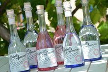 Charger l&#39;image dans la galerie, Both of our gins are pictured here in our garden on a white table: 2 Rosé Gins  in the middle in their pink bottles, surrounded by four bottles of our Original gin. French: Nos deux gins sont photographiés sur une table blanche dans notre jardin : 2 Gin Rosé au milieu dans leurs bouteilles roses, entourés de quatre bouteilles de notre Gin Original.
